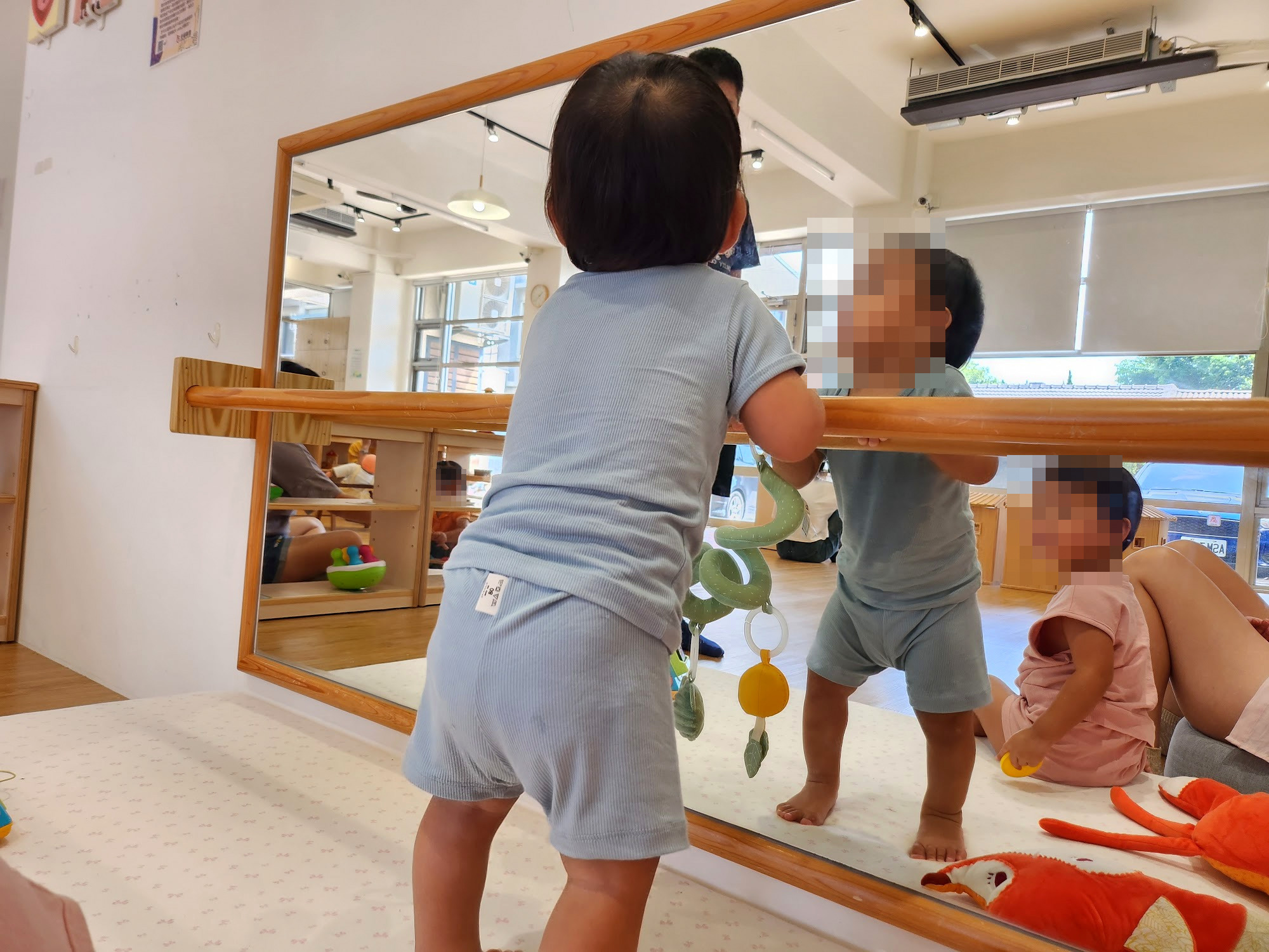 孩子扶著鏡子前的木頭扶手玩掛著的玩具