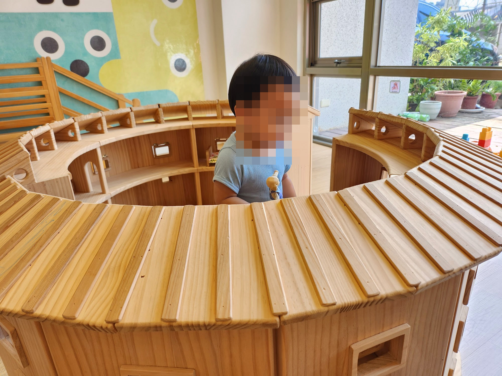 孩子在育兒+苗栗站的圓形木頭遊戲屋裡探頭