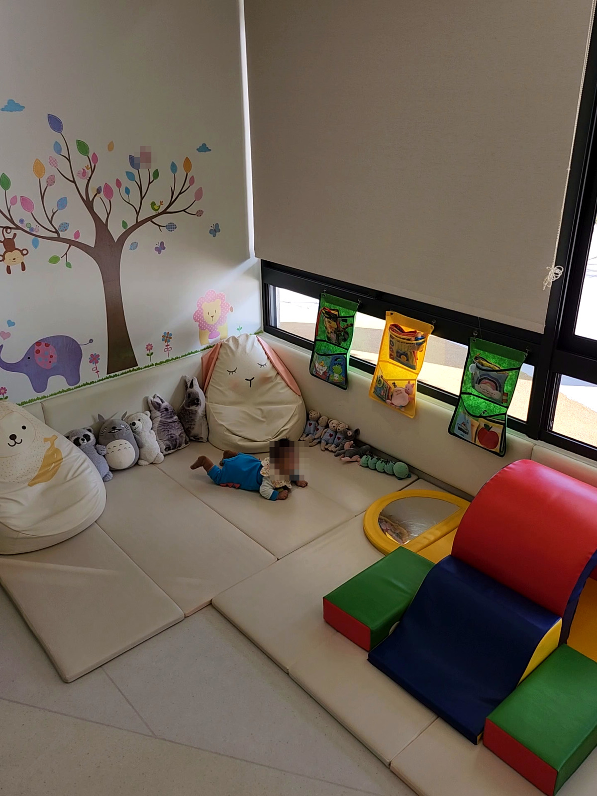 北區親子館窗邊的寶寶區,有大樹壁貼、軟墊爬坡和懶骨頭(孩子臉部已打馬賽克)