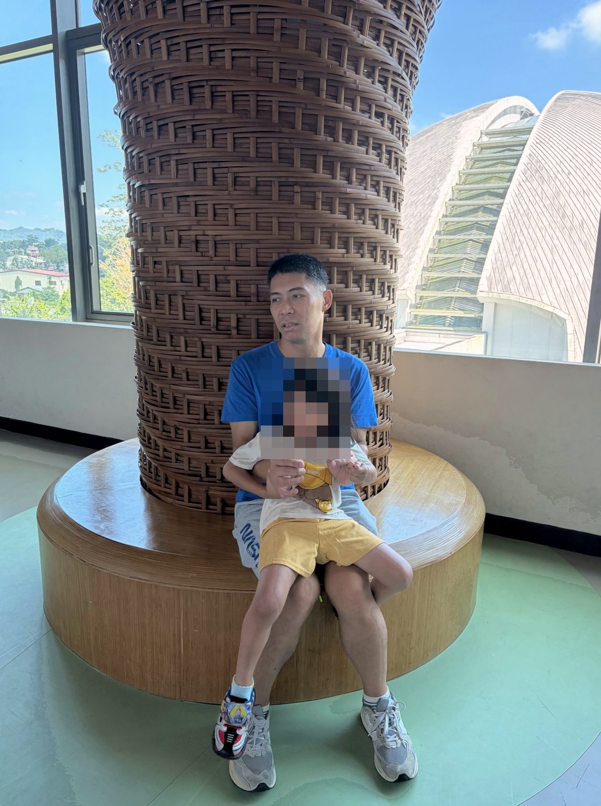 爸爸抱著芮坐在園區室內大柱子旁休息
