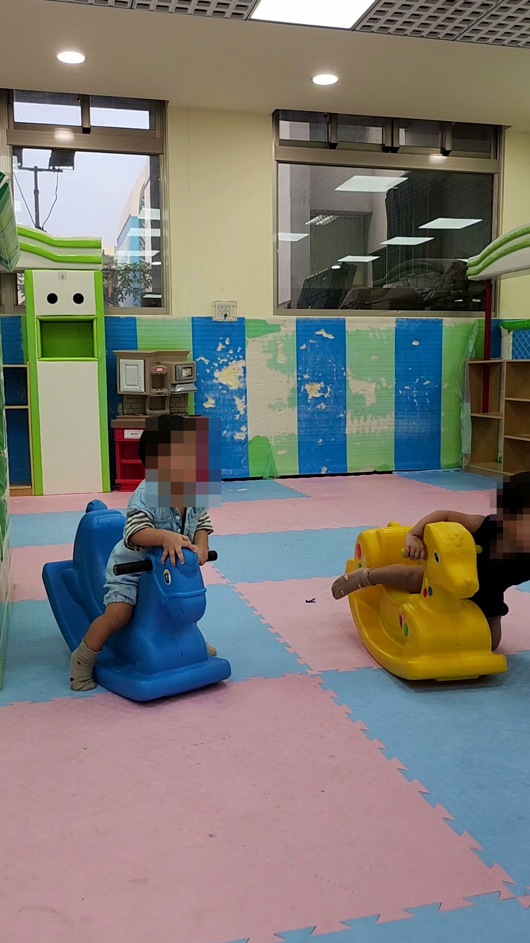 兩個孩子在兒童遊戲區玩藍色和黃色搖搖馬