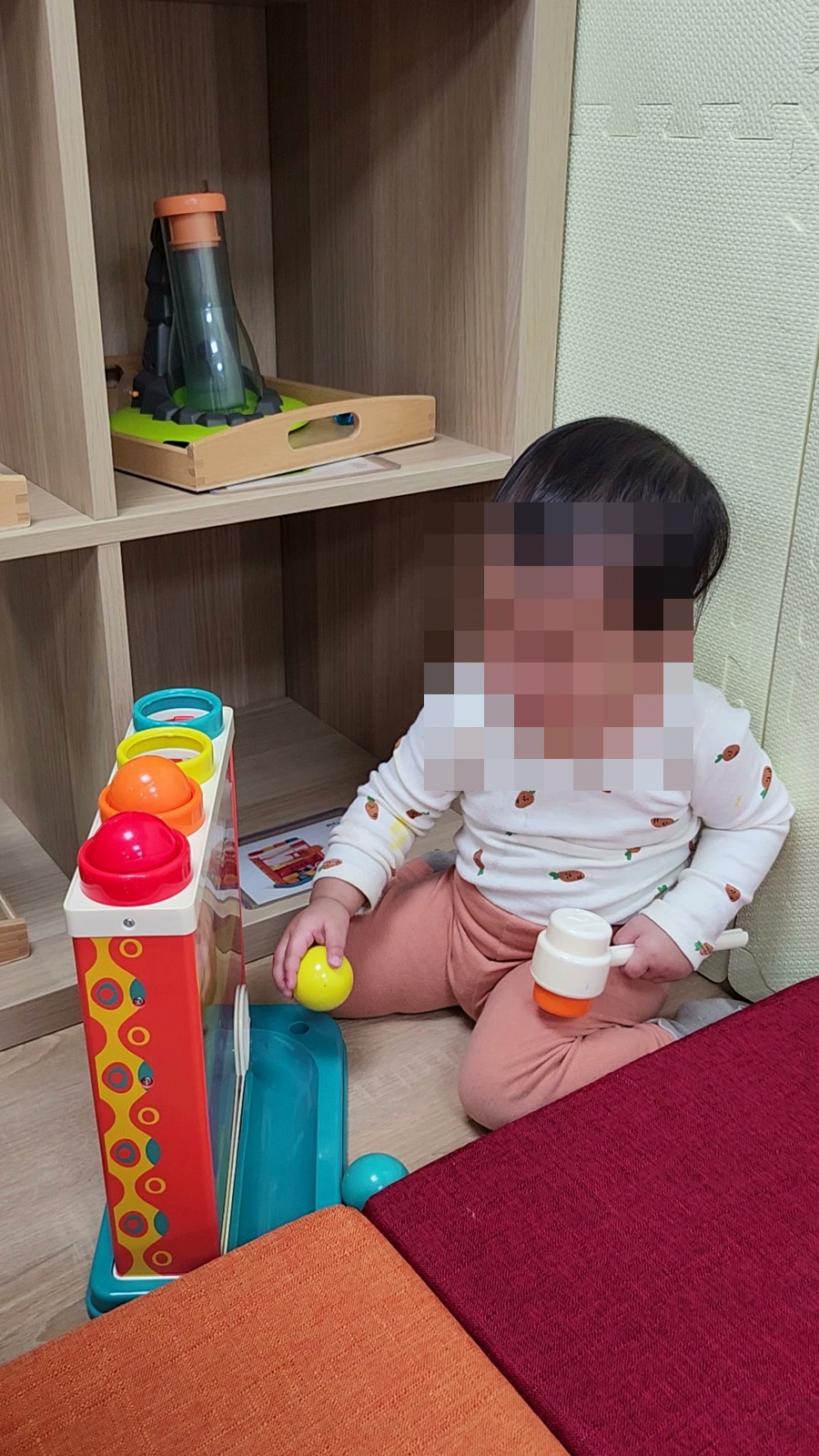 寶寶坐在書櫃旁玩玩具